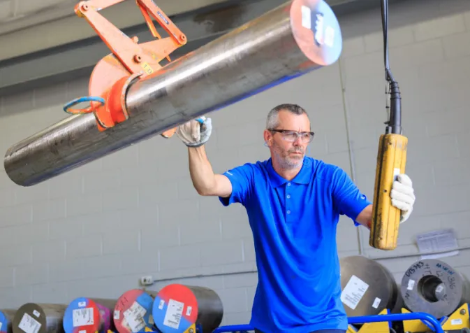 A man holding a large metal pipe in a factory