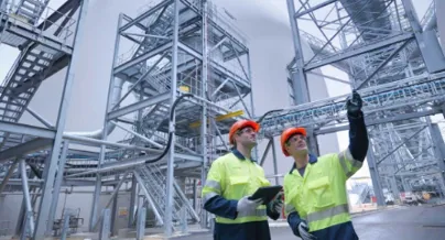 Two workers in safety gear standing in front of a large industrial building