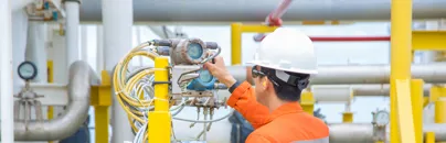 A man in an orange shirt and hard hat is working on a pipe