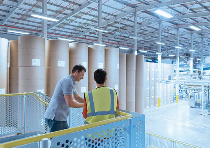 Two people standing in a warehouse with large rolls of paper
