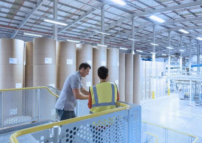Two people standing in a warehouse with large rolls of paper