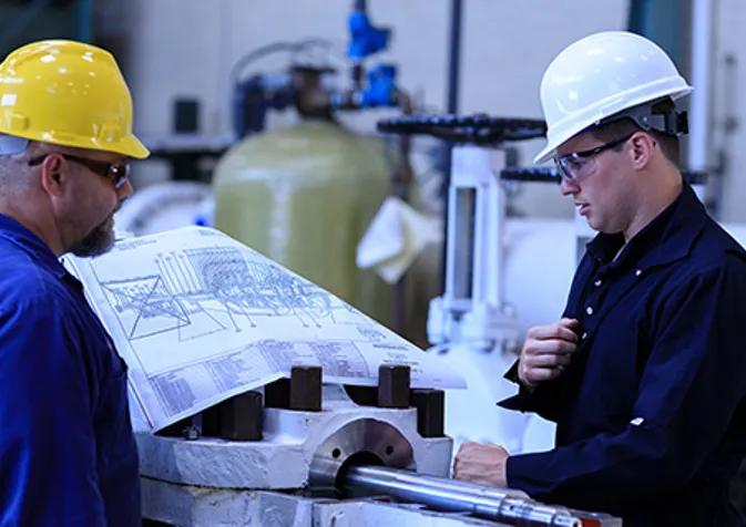 Two men in hard hats looking at a blueprint