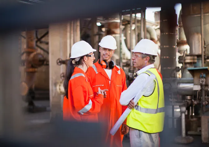 Three people in hard hats and safety vests talking to each other