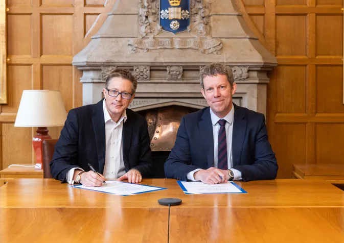 Two men in suits sitting at a table signing papers