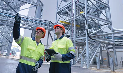 Two workers in safety gear standing in front of a large industrial building