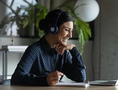 A woman wearing headphones sits at a desk with a laptop