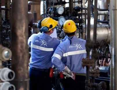 Two men in blue and yellow work clothes standing in front of a large industrial machine