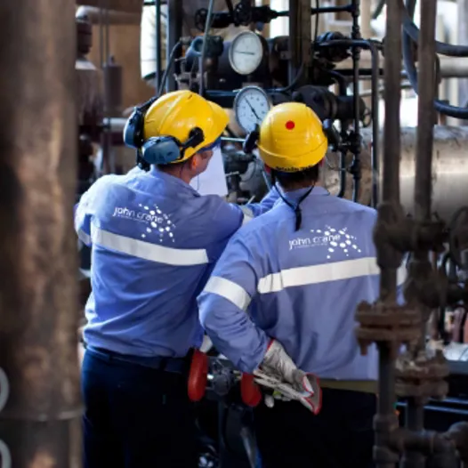 Two men in blue and yellow work clothes standing in front of a large industrial machine
