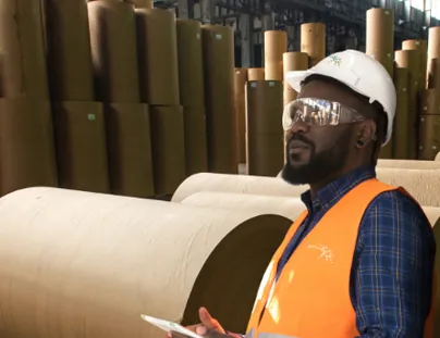 A man in an orange vest and safety glasses standing in front of rolls of paper