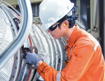 A man in an orange shirt and hard hat working on a large pipe