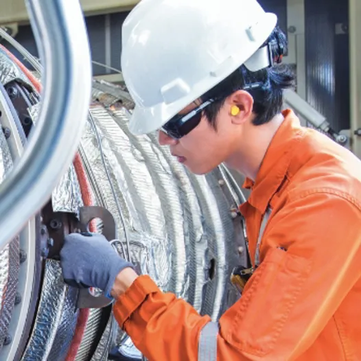 A man in an orange shirt and hard hat working on a large pipe