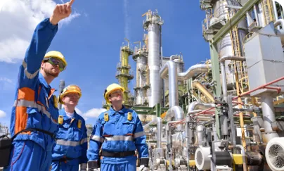 Three men in blue overalls standing in front of a refinery