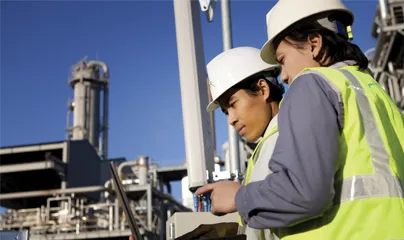 Two men in hard hats and safety vests looking at a tablet