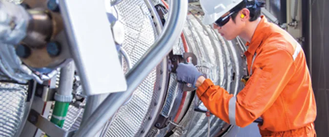 A man in an orange uniform working on a large pipe