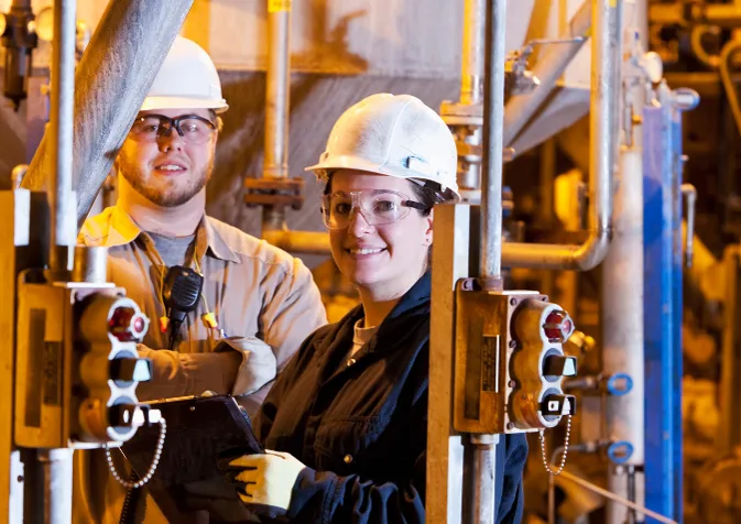 Two people in hard hats standing in a factory