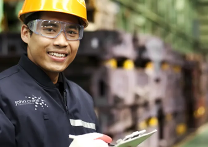 A smiling man in a factory holding a clipboard