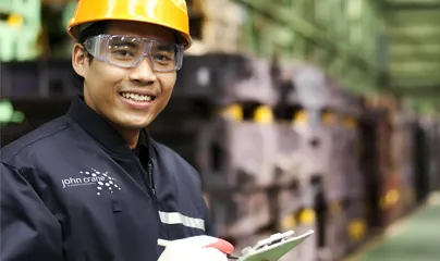 A smiling man in a factory holding a clipboard