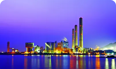 A large body of water reflecting a brightly lit industrial building at night, and a vibrant blue and purple sky
