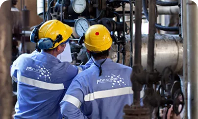 Two men in blue and yellow work clothes standing next to a large pipe