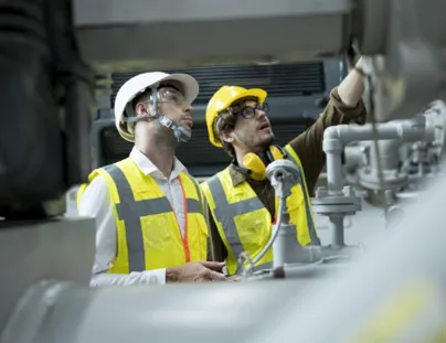 Two men in safety vests and hard hats working on a machine