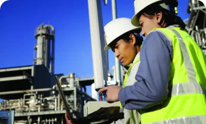 Two men in hard hats and safety vests looking at a laptop