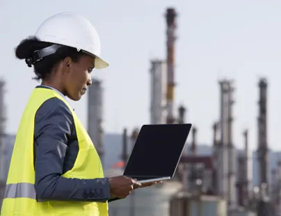 A woman in a hard hat and safety vest holding a laptop