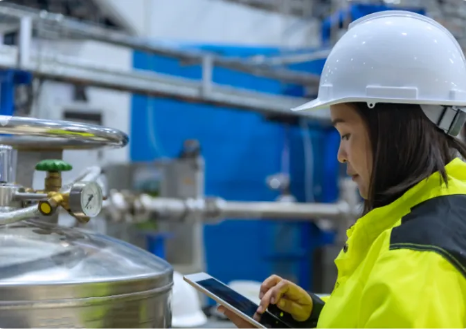 A woman in a hard hat and safety vest using a tablet